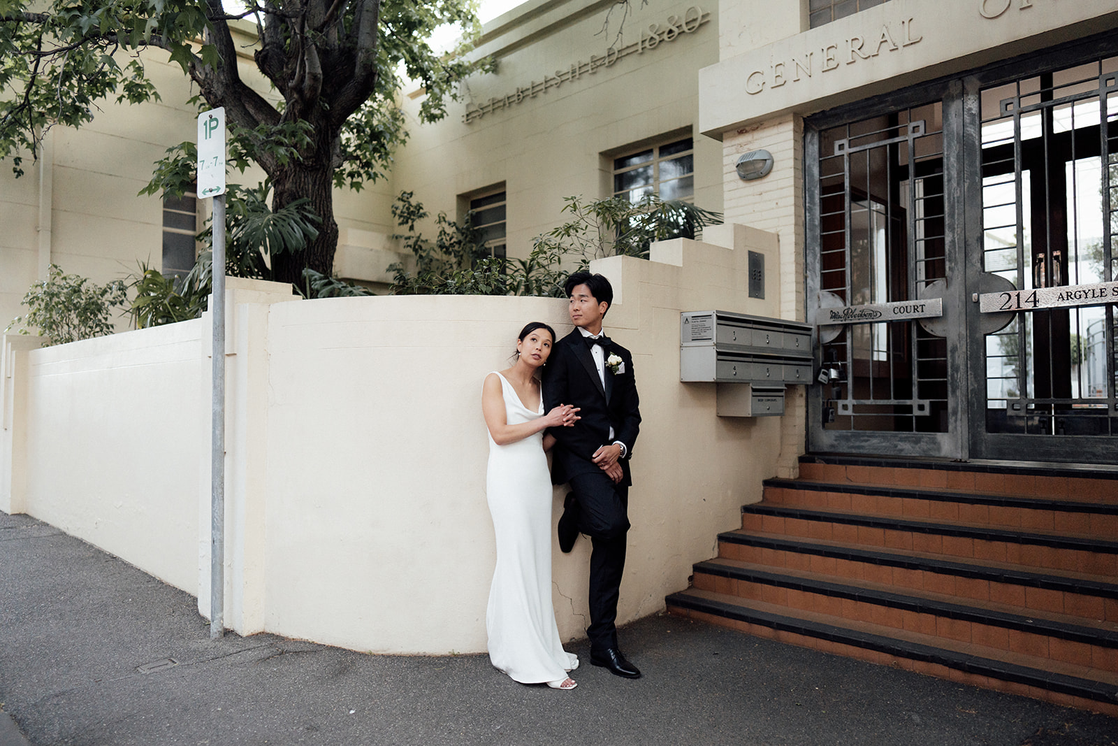Bride and groom leaning against a building in Collingwood